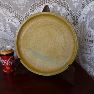 May include: A large, round, yellow ceramic plate with a speckled glaze. The plate is on a wooden stand.