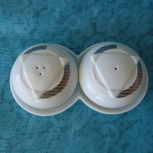 May include: White ceramic salt and pepper shakers with a geometric design. The shakers are connected by a base.