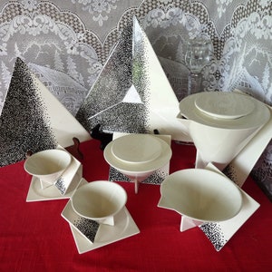 May include: A white ceramic tea set with a geometric design. The set includes a teapot, a sugar bowl, a creamer, and two cups and saucers. The pieces are decorated with black dots.