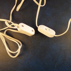 Puede incluir: Dos interruptores blancos en l&iacute;nea con cables blancos. Los interruptores est&aacute;n sobre una superficie azul oscuro.