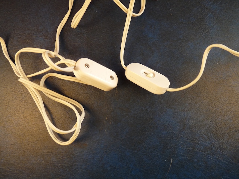 Puede incluir: Dos interruptores blancos en l&iacute;nea con cables blancos. Los interruptores est&aacute;n sobre una superficie azul oscuro.