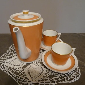 Könnte beinhalten: Ein vintage Kaffeekanne-Set in Orange und Weiß mit goldenen Verzierungen. Das Set enthält eine Kaffeekanne, zwei Tassen und zwei Untertassen.