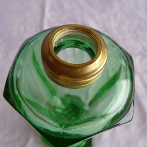 May include: A green glass oil lamp with a brass top. The lamp has a hexagonal shape and a textured surface.