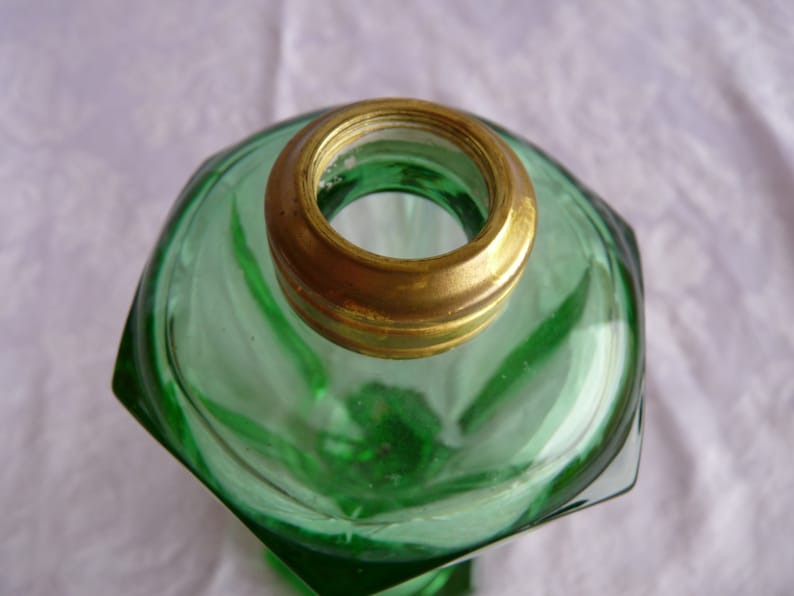 May include: A green glass oil lamp with a brass top. The lamp has a hexagonal shape and a textured surface.