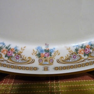 May include: Cream-colored oval serving platter with a floral border. The border features bouquets of pink, orange, and blue flowers, with gold and gray accents. The edge has a gold trim.
