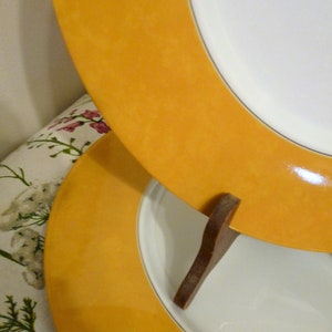 Puede incluir: Dos platos de cerámica amarillos apilados uno encima del otro. Los platos tienen un centro blanco y un borde amarillo. Los platos están sobre un soporte de madera.