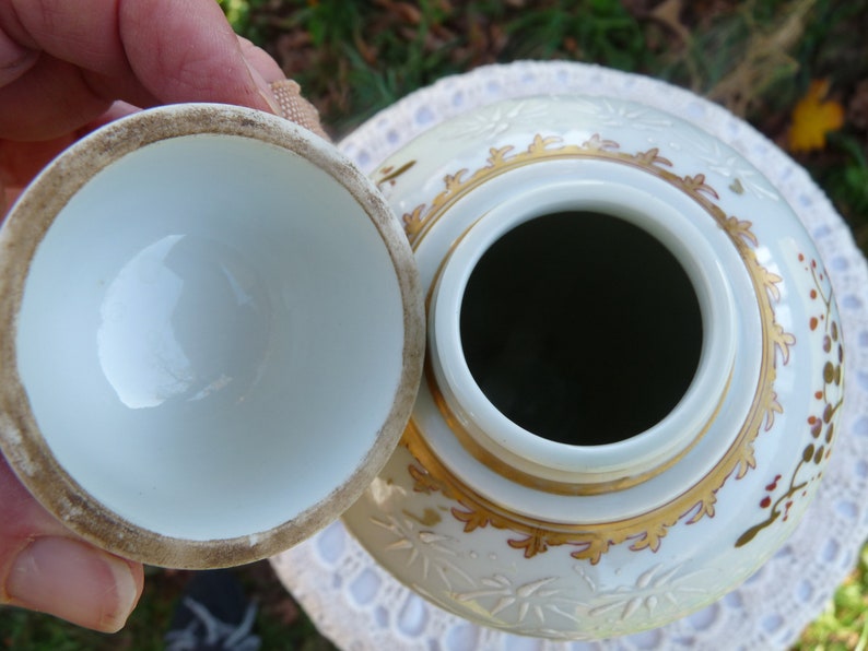 May include: A white porcelain jar with a lid, decorated with gold and red floral patterns. The jar has a wide opening and a smooth, white interior.