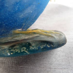 Pode incluir: Close-up da base de uma escultura de vidro azul com uma base amarela e verde. A escultura &eacute; assinada "R. Lalique".