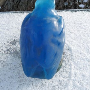 Pode incluir: Uma figurinha de p&aacute;ssaro de vidro azul com um acabamento liso e brilhante. O p&aacute;ssaro est&aacute; empoleirado em uma superf&iacute;cie branca.