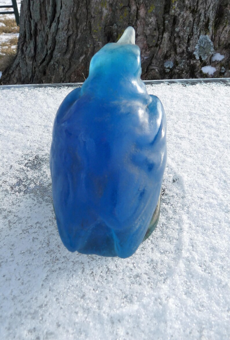 Pode incluir: Uma figurinha de p&aacute;ssaro de vidro azul com um acabamento liso e brilhante. O p&aacute;ssaro est&aacute; empoleirado em uma superf&iacute;cie branca.