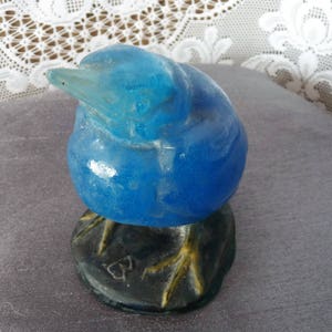 Pode incluir: Uma figurinha de p&aacute;ssaro de vidro azul com p&eacute;s amarelos e uma base preta. O p&aacute;ssaro est&aacute; empoleirado em uma rocha com um pequeno desenho em forma de cora&ccedil;&atilde;o.