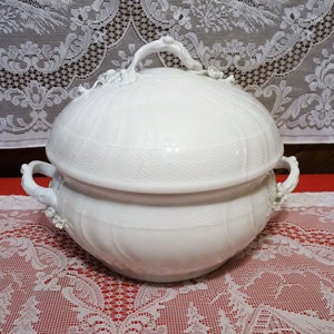 May include: A white porcelain serving dish with a lid. The dish has a decorative design and is perfect for serving a variety of foods.