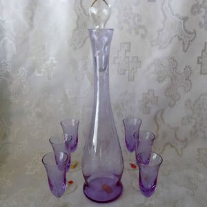 May include: A vintage purple glass decanter set with a tall, slender decanter and six matching stemmed glasses. The decanter has a clear glass stopper. The glasses and decanter are a soft purple color, perfect for serving beverages.