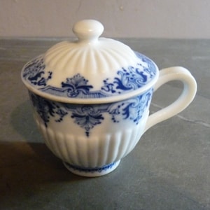 May include: A white porcelain creamer with a blue and white floral design. The creamer has a lid and a handle.