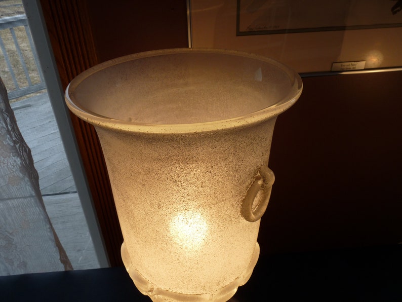 Puede incluir: Una pantalla de l&aacute;mpara de vidrio esmerilado con un asa decorativa. La pantalla est&aacute; iluminada desde el interior, proyectando un brillo c&aacute;lido.