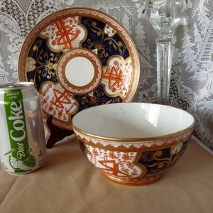 May include: A vintage porcelain teacup and saucer set with a blue and gold floral pattern. The saucer has a raised rim and the cup has a wide, shallow bowl. The set is in excellent condition.