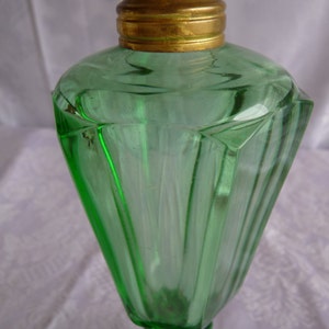 May include: A green glass oil lamp with a brass top and a faceted design. The lamp has a wide base and a narrow neck.