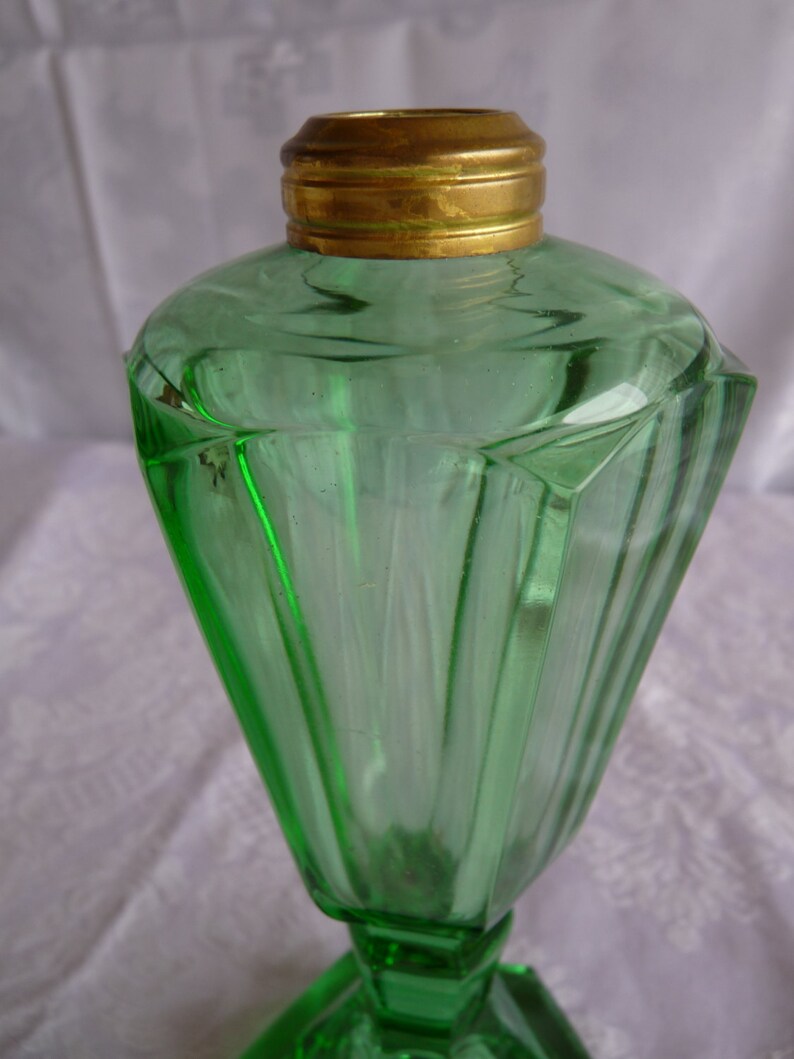 May include: A green glass oil lamp with a brass top and a faceted design. The lamp has a wide base and a narrow neck.