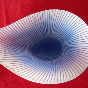 May include: A white glass bowl with a blue and white striped design. The bowl is shaped like a seashell and has a deep, rounded center.