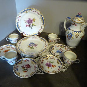 May include: A vintage porcelain tea set with floral patterns in shades of blue, pink, and yellow. The set includes a teapot, cups, saucers, and a larger plate.