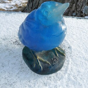 Pode incluir: Uma figurinha de p&aacute;ssaro de vidro azul com uma base detalhada. O p&aacute;ssaro est&aacute; empoleirado em uma base texturizada com uma pequena inscri&ccedil;&atilde;o indistinta.