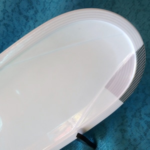 Pode incluir: Prato de servir de cerâmica branca com um design geométrico cinza e branco. O prato tem uma forma arredondada e uma borda ligeiramente elevada.