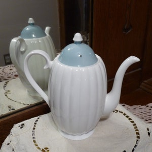 Puede incluir: Cafetera de cerámica blanca con tapa azul claro y diseño acanalado. La cafetera tiene un asa y un pico.