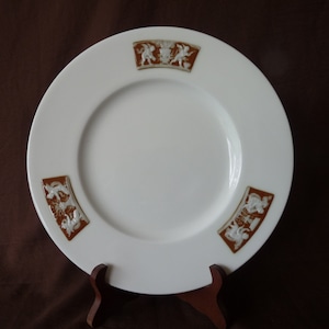 May include: White ceramic plate with a brown rim and four decorative cherub figures in relief. The cherubs are holding a banner with the word "Amour" written on it.