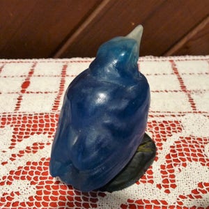 Pode incluir: Uma figurinha de p&aacute;ssaro de vidro azul com um acabamento liso e brilhante. O p&aacute;ssaro est&aacute; empoleirado em uma pequena base cinza escura.