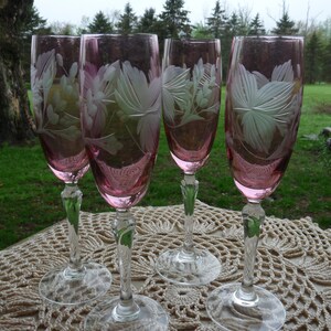 May include: Set of four pink etched glass champagne flutes with a floral design. The flutes are on a white crocheted doily.