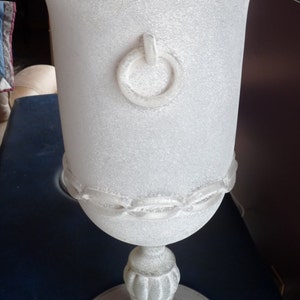 Puede incluir: Dos l&aacute;mparas de vidrio blanco esmerilado con un detalle de anillo en el cuerpo y una base texturizada. Las l&aacute;mparas est&aacute;n sobre una superficie azul oscuro.