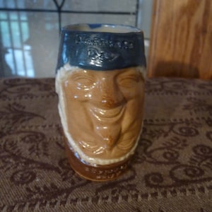 May include: A ceramic mug shaped like a man's head with a blue hat that says "St. Patrick's Day".