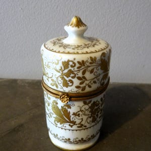 May include: A white porcelain trinket box with a gold lid and floral design. The box has a hinged lid with a gold trim.