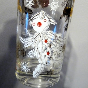 Könnte beinhalten: Ein klares Glas mit einem weißen und goldenen Design. Das Design zeigt einen Schneemann mit Stechpalmenblättern und roten Beeren. Das Glas hat ein Schneeflockenmuster.
