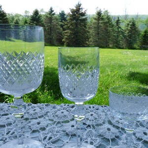 Puede incluir: Tres copas de vidrio transparente con un patrón de diamante. Las copas están dispuestas en una fila de la más grande a la más pequeña sobre un mantel de encaje blanco.