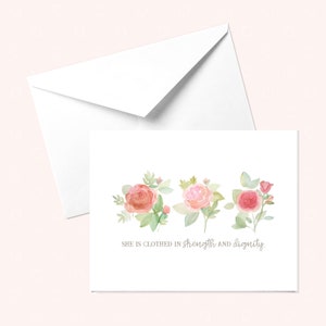 Puede incluir: Una tarjeta blanca con tres rosas rosadas de acuarela y hojas verdes. El texto "Ella está vestida de fuerza y dignidad." está impreso en gris debajo de las rosas.