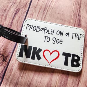 May include: White luggage tag with black text that reads "Probably on a trip to see NK  ♥ TB". The tag has a black strap.