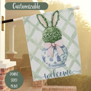 May include: A green topiary bunny in a blue and white planter with a pink gingham bow. The planter is on a green and white checkered background. The text "welcome" is written in cursive below the planter.