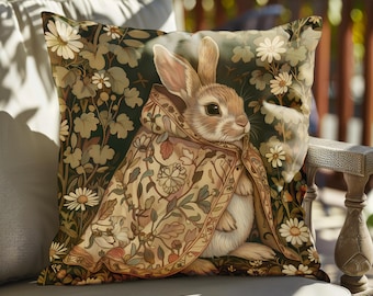 May include: Square decorative pillow featuring a detailed illustration of a rabbit wearing a floral patterned cloak. The pillow has a dark green background with white daisies and other floral elements. The rabbit is light brown with long ears.