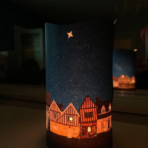 May include: A felt nightlight with a star and a row of houses with lit windows against a dark blue background.
