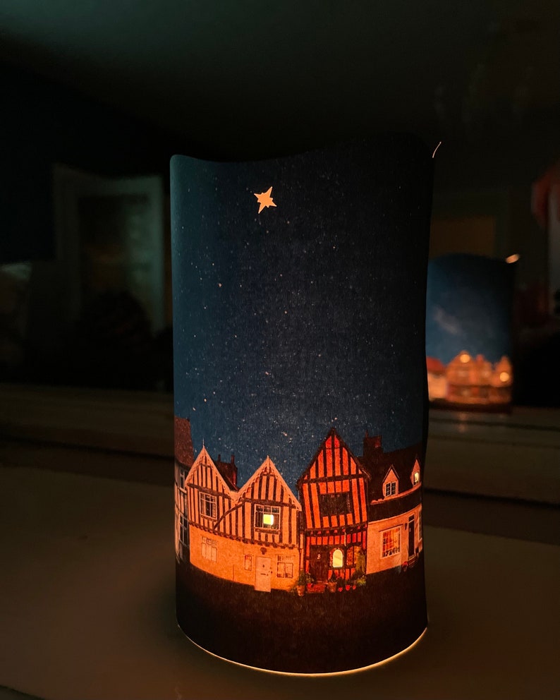 May include: A felt nightlight with a star and a row of houses with lit windows against a dark blue background.