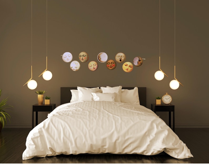 K&ouml;nnte beinhalten: Ein Schlafzimmer mit einem Bett mit wei&szlig;er Bettw&auml;sche, flankiert von schwarzen Nachttischen. &Uuml;ber dem Bett befindet sich eine Sammlung von Wandkunst mit Mondgesichtern. Goldene Pendelleuchten h&auml;ngen von der Decke, und eine kleine Uhr steht auf einem Nachttisch.