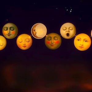 Puede incluir: Una cadena de luces decorativas con forma de luna con diferentes expresiones faciales. Las lunas son en tonos de amarillo, naranja y blanco, con mejillas rosadas y ojos cerrados. El fondo es un cielo nocturno oscuro con estrellas.