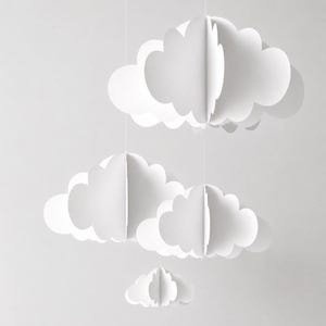 May include: A hanging mobile featuring four white paper clouds of varying sizes. Each cloud is constructed from multiple intersecting flat planes to create a three-dimensional, layered effect. The clouds are suspended by thin, vertical white strings.