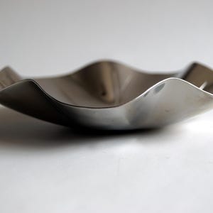 Puede incluir: Un cuenco de metal plateado con una forma ondulada y org&aacute;nica. El cuenco est&aacute; vac&iacute;o y tiene una superficie reflectante.