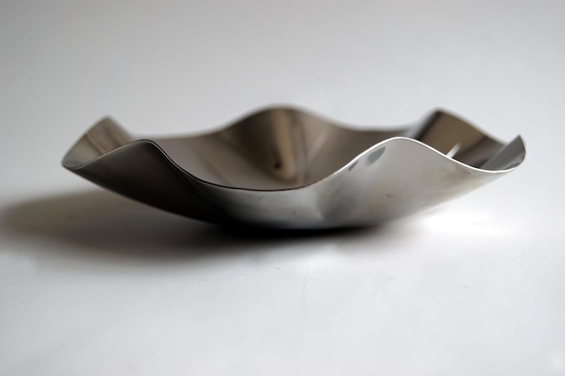 Puede incluir: Un cuenco de metal plateado con una forma ondulada y org&aacute;nica. El cuenco est&aacute; vac&iacute;o y tiene una superficie reflectante.