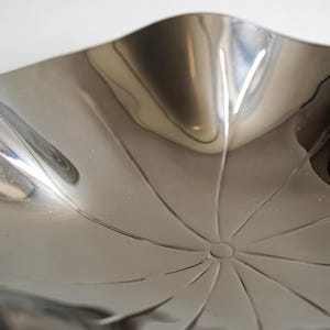 Puede incluir: Un cuenco de metal plateado con una forma ondulada org&aacute;nica y un dise&ntilde;o de estrella en el centro.