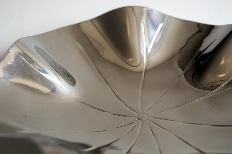 Puede incluir: Un cuenco de metal plateado con una forma ondulada org&aacute;nica y un dise&ntilde;o de estrella en el centro.
