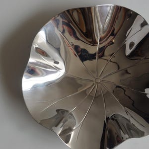 Puede incluir: Un cuenco decorativo de plata brillante con forma de flor y un centro texturizado. El cuenco est&aacute; hecho de metal y tiene una superficie lisa y reflectante.