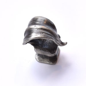 May include: A silver metal sculpture of a stylized leaf, with a textured surface. The sculpture is on a white background.